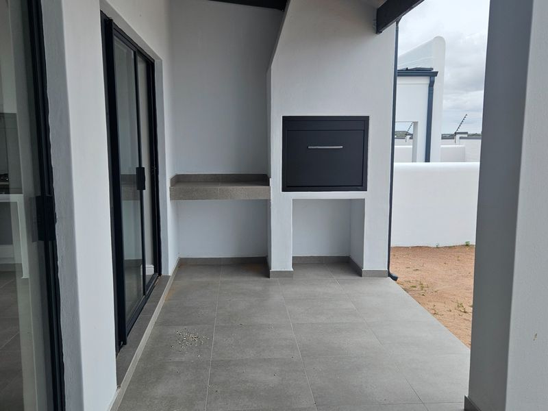 A modern covered patio featuring a built-in braai, concrete prep counter, and tiled flooring, providing a clean outdoor entertainment space.