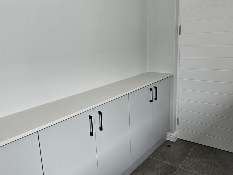 A clean, modern scullery or utility area featuring sleek built-in cabinetry with stone countertops and neutral tiled flooring.