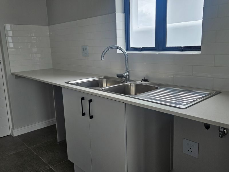 A clean, modern scullery featuring a double basin stainless steel sink, quartz countertops, subway tile backsplash, and ample built-in cabinetry.
