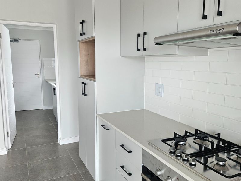 Modern kitchen featuring light grey cabinetry, stone countertops, subway tile backsplash, and integrated gas hob with extractor fan.