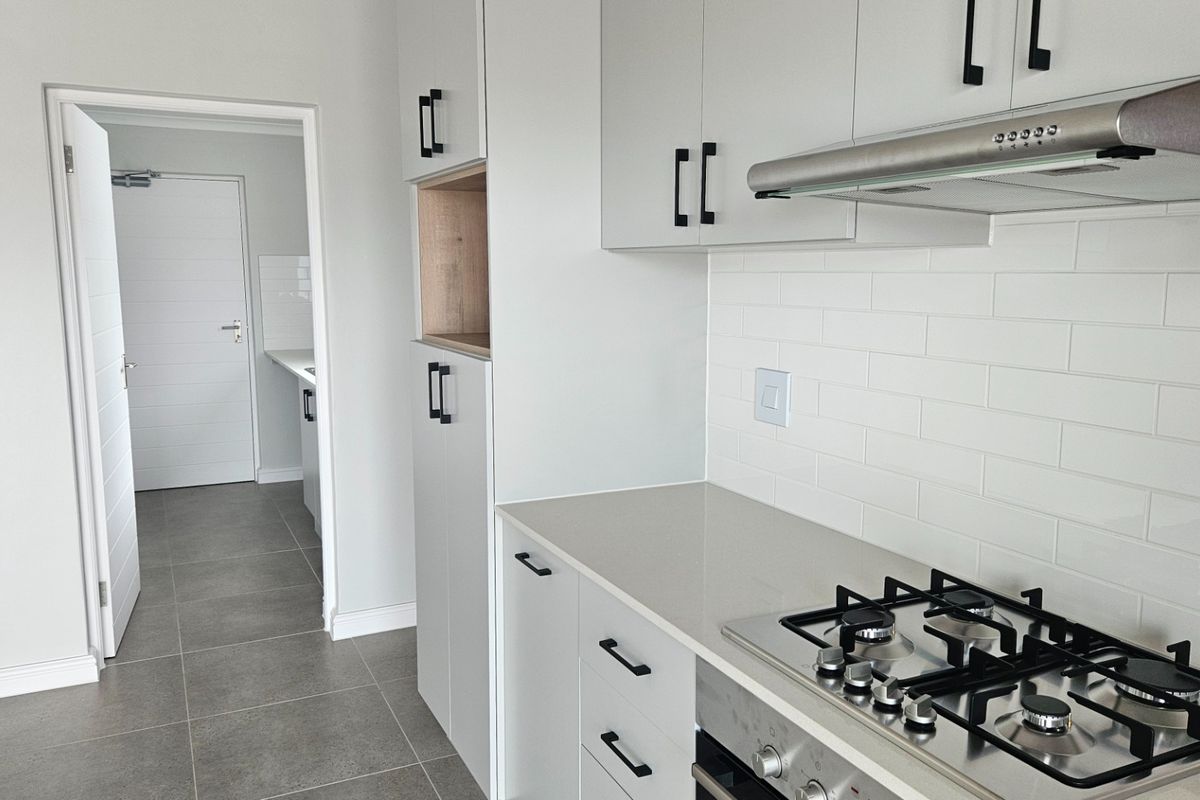 Modern kitchen featuring light grey cabinetry, stone countertops, subway tile backsplash, and integrated gas hob with extractor fan.