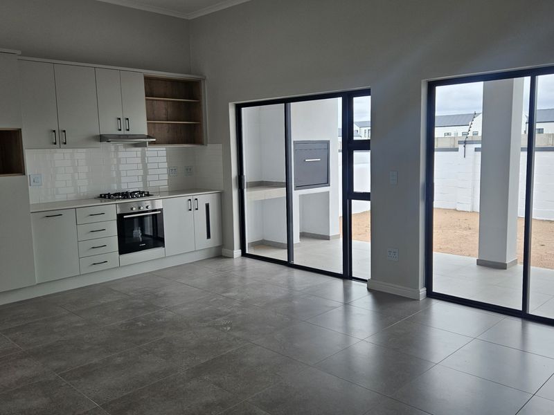 Modern open-plan kitchen featuring sleek cabinetry, integrated appliances, and large sliding doors leading to a covered patio with a built-in braai.