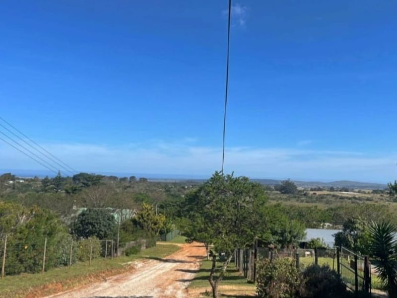 A view of an unpaved access road leading through a residential area with overhead power lines and surrounding natural landscape.