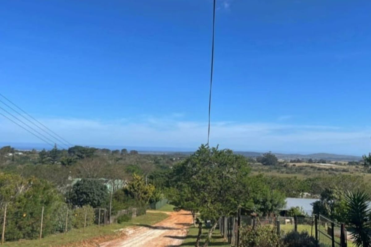 A view of an unpaved access road leading through a residential area with overhead power lines and surrounding natural landscape.