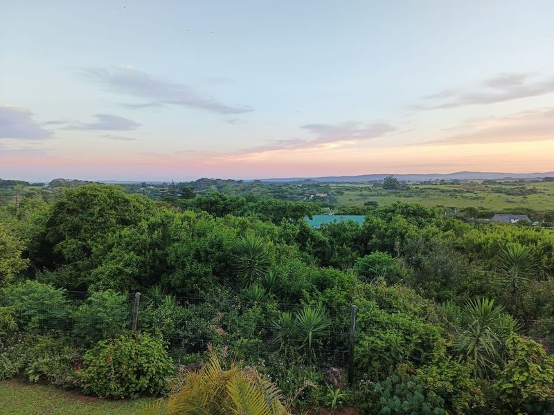 A scenic elevated view overlooking lush green vegetation and rolling hills under a soft sunset sky.