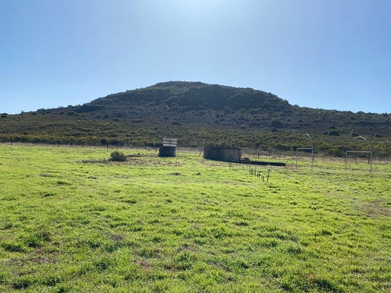Expansive farm landscape featuring open grazing land, wire fencing, and a weathered water reservoir with a scenic mountain backdrop.