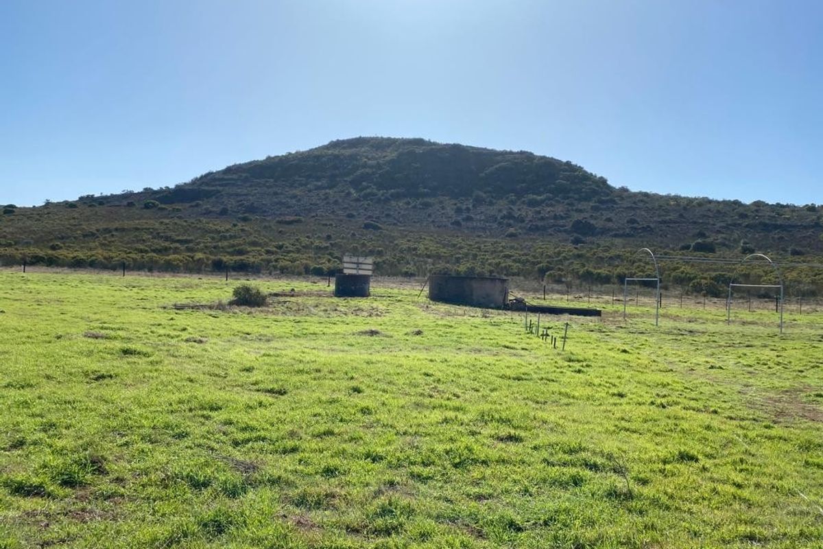 Expansive farm landscape featuring open grazing land, wire fencing, and a weathered water reservoir with a scenic mountain backdrop.