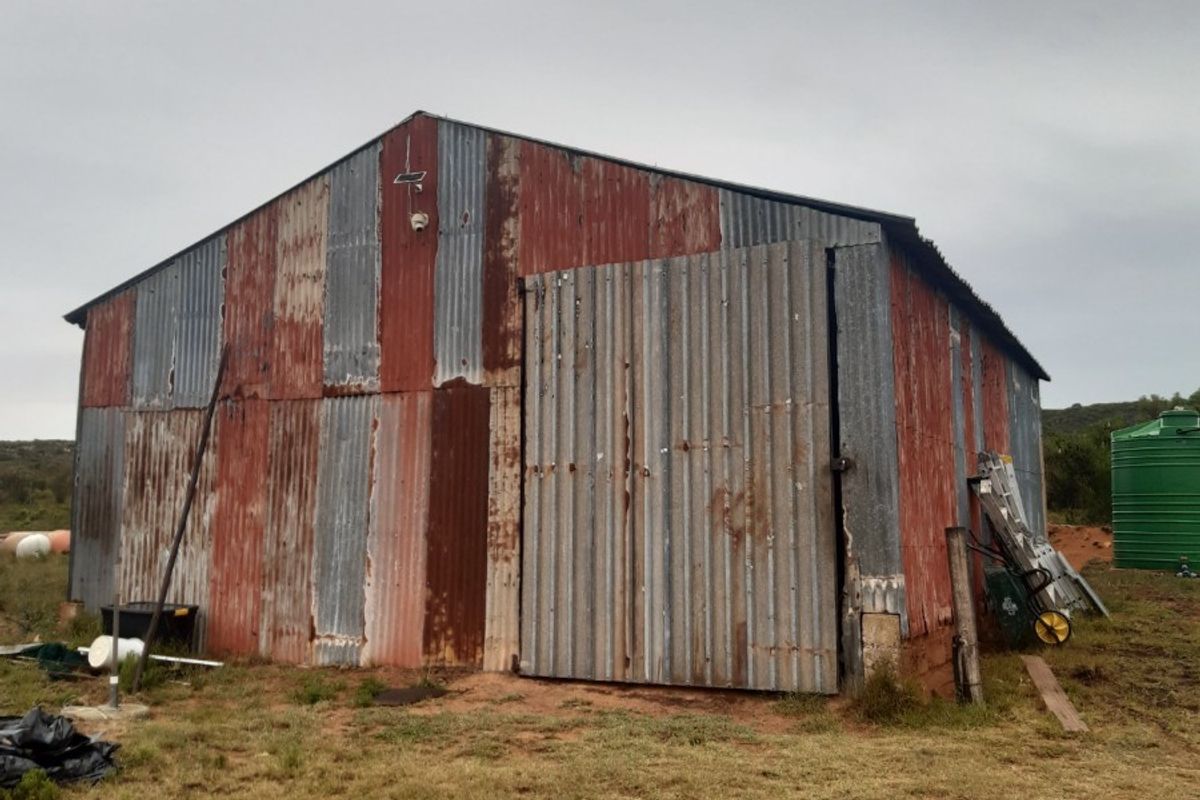 A rustic farm outbuilding featuring corrugated iron cladding with visible signs of age and weathering, including a large sliding door and adjacent water tank.