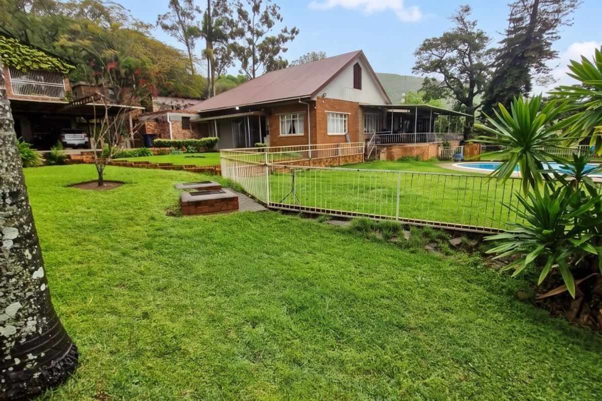 Rear view of a brick farmhouse featuring a spacious lawn, swimming pool, built-in fire pit, and a covered patio area.