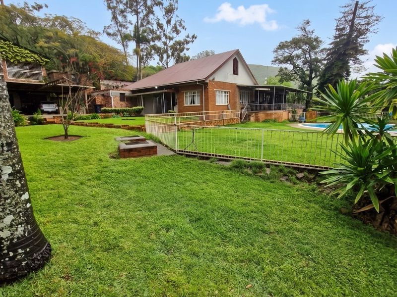 Rear view of a brick farmhouse featuring a spacious lawn, swimming pool, built-in fire pit, and a covered patio area.
