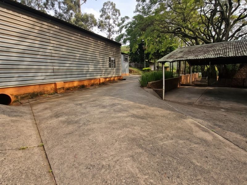 Exterior view of a farm property featuring a large corrugated metal shed, concrete driveway, and a covered carport area.