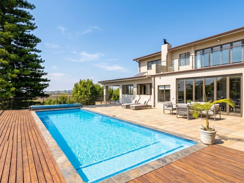 A well-maintained outdoor pool area featuring a swimming pool, timber decking, stone patio, and glass balustrades, offering a seamless transition to the rear facade.