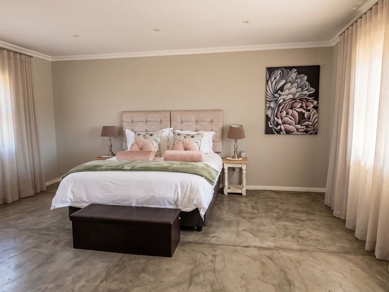 Spacious bedroom featuring polished concrete flooring, neutral wall tones, and dual windows with floor-to-ceiling curtains, creating a bright and modern atmosphere.