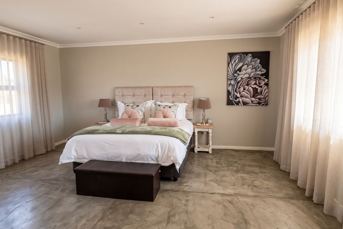 Spacious bedroom featuring polished concrete flooring, neutral wall tones, and dual windows with floor-to-ceiling curtains, creating a bright and modern atmosphere.