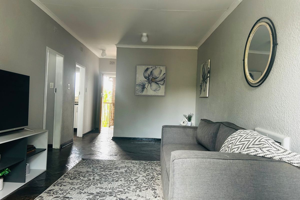 A living room featuring neutral grey walls, coved ceilings, and dark flooring, providing a functional and well-lit space with access to adjacent rooms.