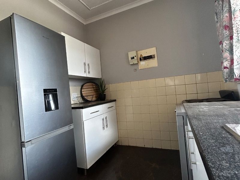 A functional kitchen featuring white cabinetry, tiled backsplash, and dark countertops, providing a practical workspace with essential built-in storage and utility access.