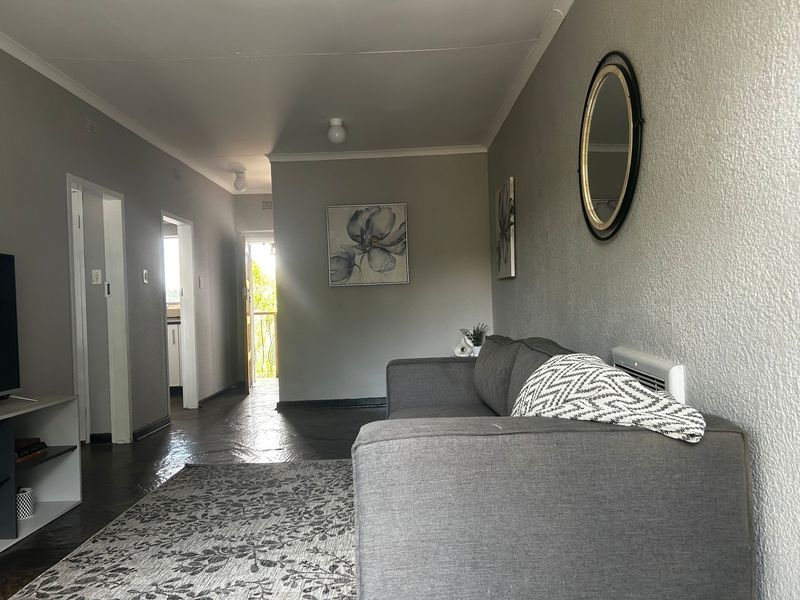 A living room featuring tiled flooring, coved ceilings, and a wall-mounted electric heater, with direct access to an adjacent hallway and exterior balcony.