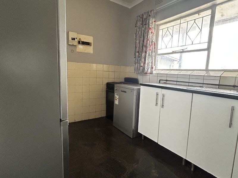 A functional kitchen featuring built-in cabinetry, a tiled splashback, and a sink, offering potential for modernization and cosmetic updates.