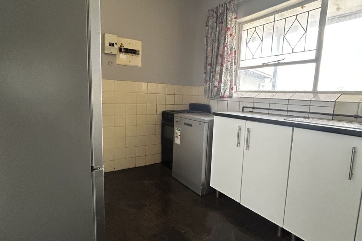 A functional kitchen featuring built-in cabinetry, a tiled splashback, and a sink, offering potential for modernization and cosmetic updates.