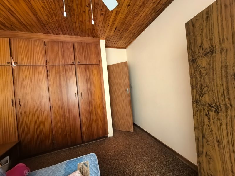 A bedroom featuring built-in wooden cupboards, a classic wooden tongue and groove ceiling, and carpeted flooring.