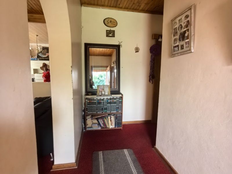 A residential hallway featuring a timber tongue and groove ceiling, arched architectural detailing, and carpeted flooring leading into the main living area.