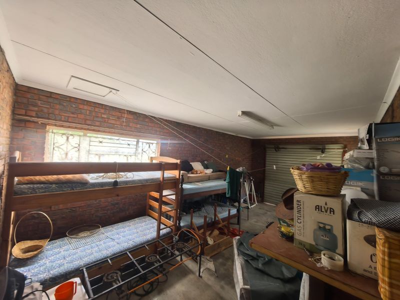 A functional garage space featuring exposed brick walls, a roll-up door, and a ceiling access hatch, currently used for storage and sleeping.