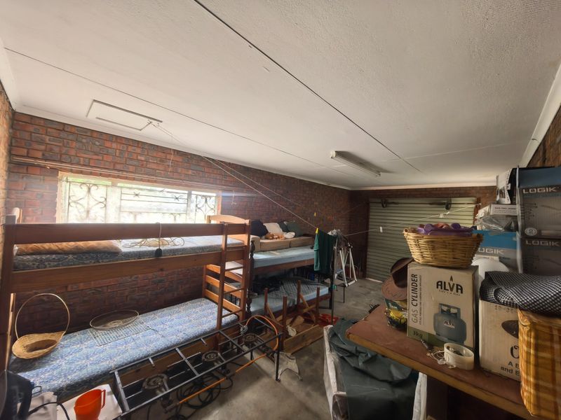 A functional garage space featuring exposed brick walls, a roller shutter door, and a ceiling access hatch, currently used for storage and sleeping.