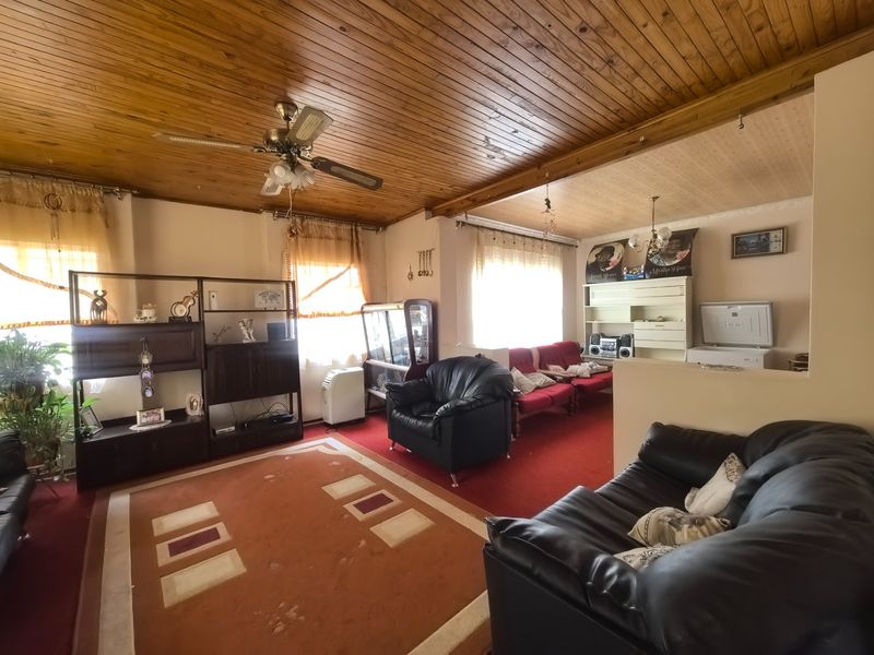 Spacious living area featuring a distinctive timber tongue and groove ceiling, ceiling fan, and built-in shelving, offering a dated but functional layout.