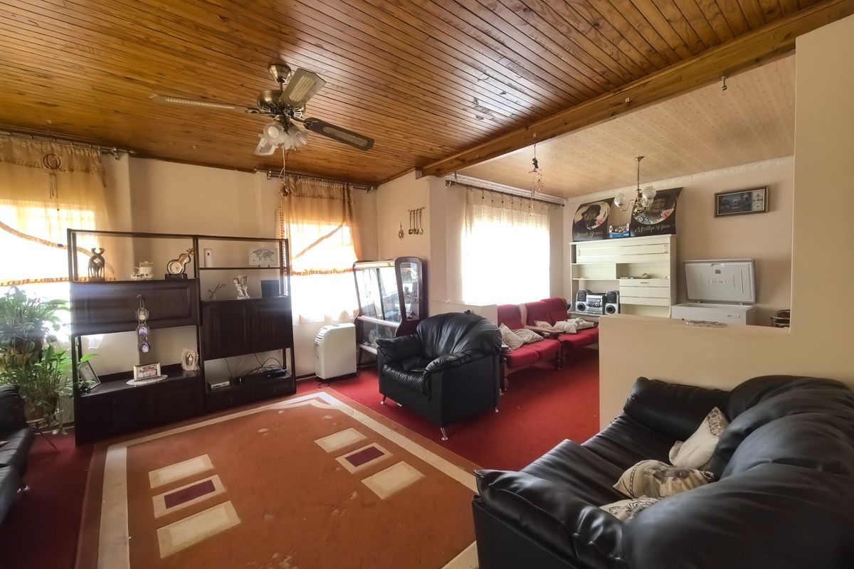 Spacious living area featuring a distinctive timber tongue and groove ceiling, ceiling fan, and built-in shelving, offering a dated but functional layout.