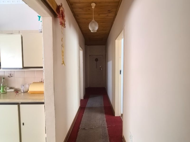 A long hallway featuring a timber-clad ceiling and carpeted flooring, providing access to adjacent rooms including the kitchen area.