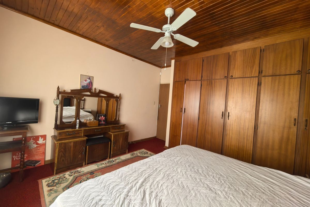 A bedroom featuring extensive built-in wooden cabinetry, a classic wooden tongue and groove ceiling, and a central ceiling fan.
