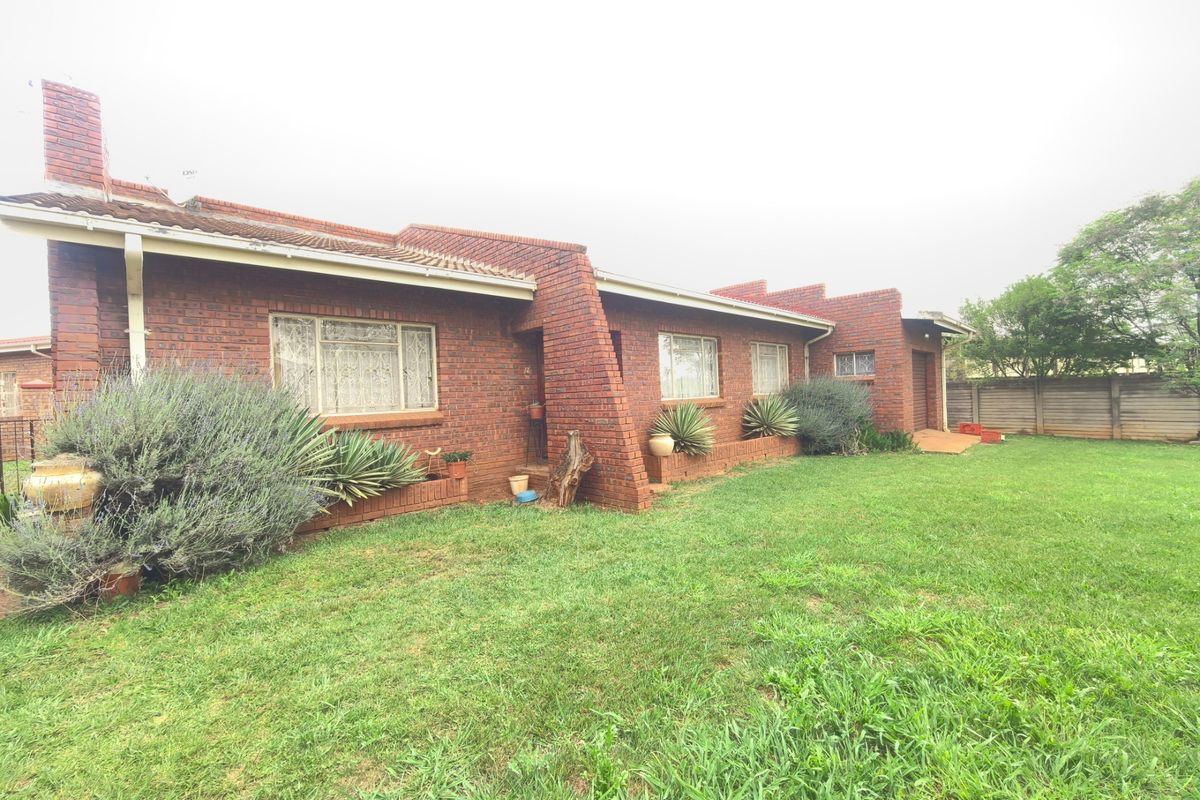 A view of the rear exterior of a face brick house featuring a tiled roof, chimney, and a spacious lawn area with boundary walling.