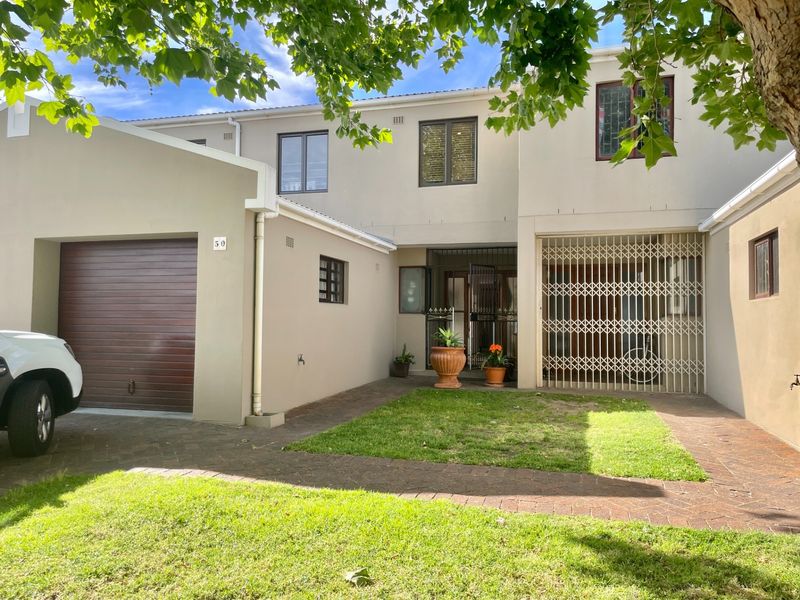 Front elevation of a townhouse featuring a single garage, paved driveway, small lawn area, and secure entrance gate.