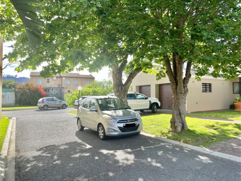 Street view of the townhouse complex showing the driveway, garage access, and established garden landscaping.