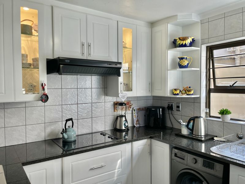 A well-maintained kitchen featuring white cabinetry, granite countertops, a tiled backsplash, and an integrated hob with an extractor fan.