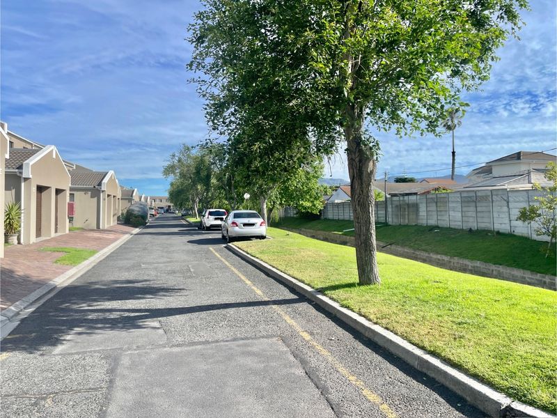 A view of the residential street within the townhouse complex, featuring paved roads, manicured verges, and established boundary walls.