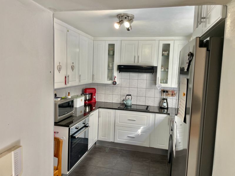 A functional kitchen featuring white cabinetry, black granite countertops, a built-in oven, electric hob, and tiled flooring.
