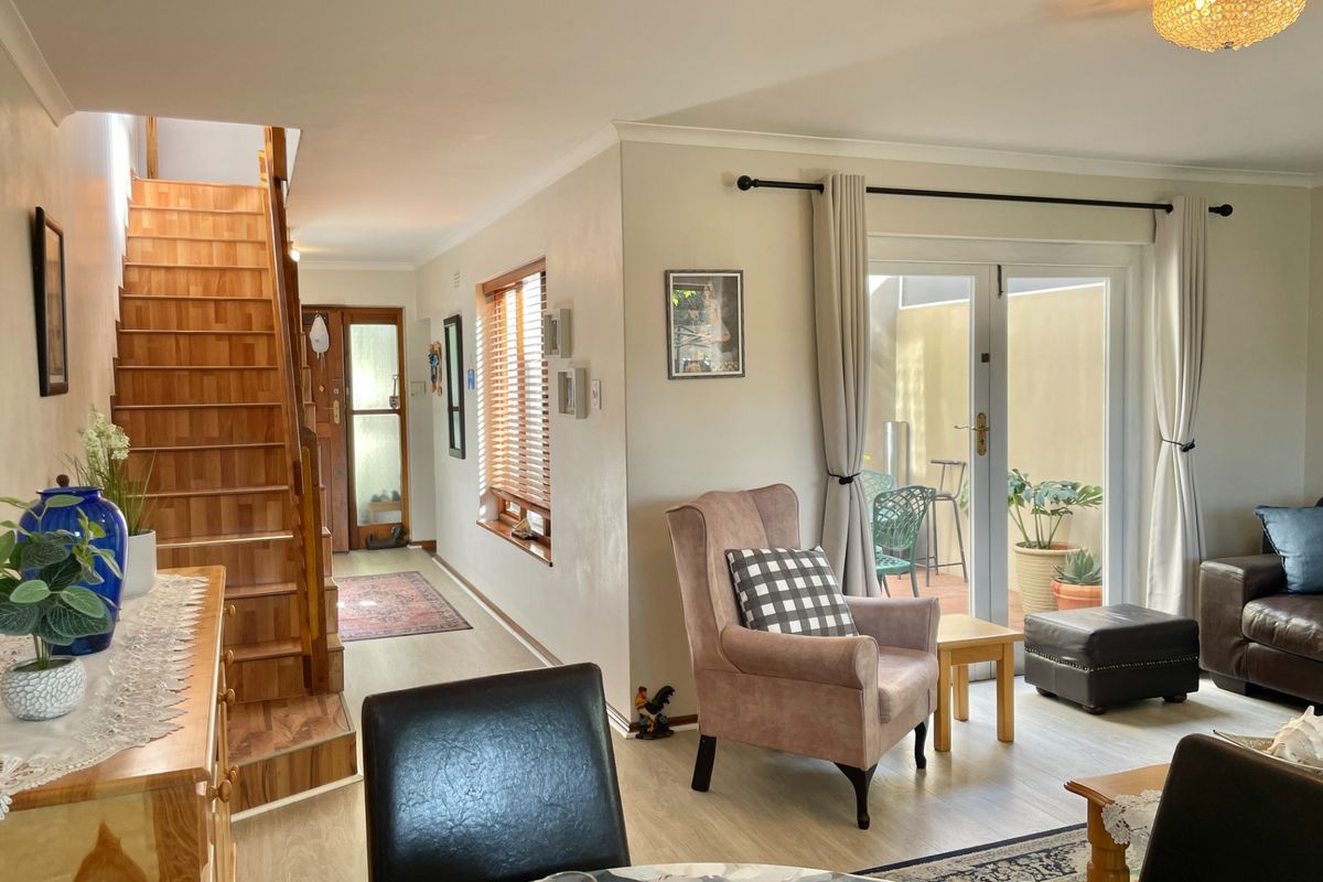 Open-plan living area featuring a wooden staircase, laminate flooring, and double french doors leading to a private patio space.
