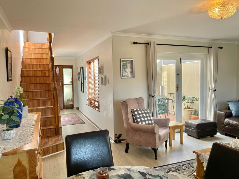 Open-plan living area featuring a wooden staircase, laminate flooring, and double french doors leading to a private patio space.