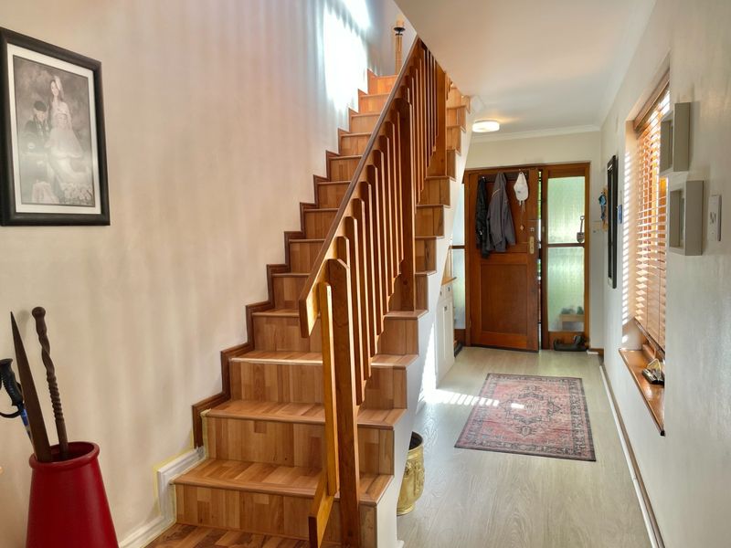 A bright entrance hall featuring a wooden staircase with a timber balustrade, laminate flooring, and a solid timber front door with glass panels.
