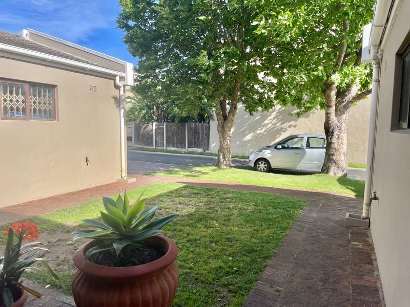 A private rear garden area featuring brick paved pathways, established trees, and a well-maintained lawn, providing a pleasant outdoor space for the townhouse.