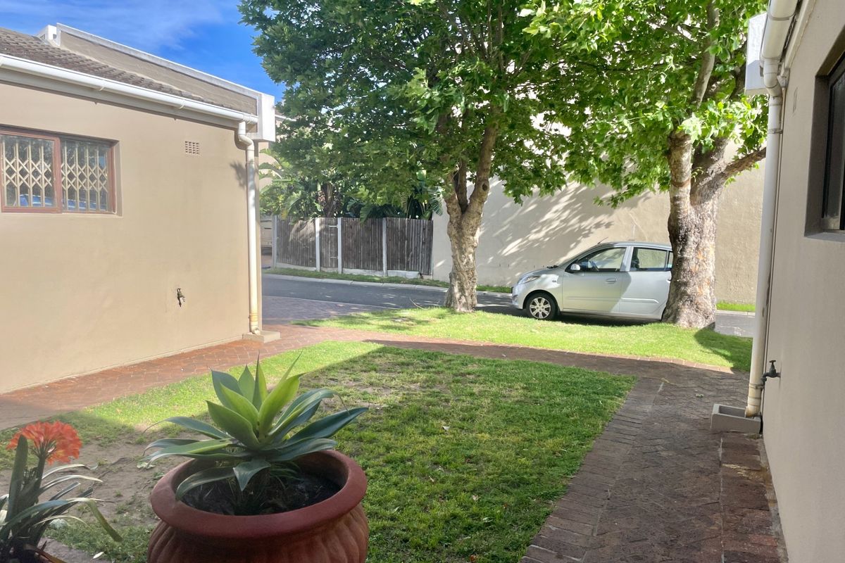 A private rear garden area featuring brick paved pathways, established trees, and a well-maintained lawn, providing a pleasant outdoor space for the townhouse.