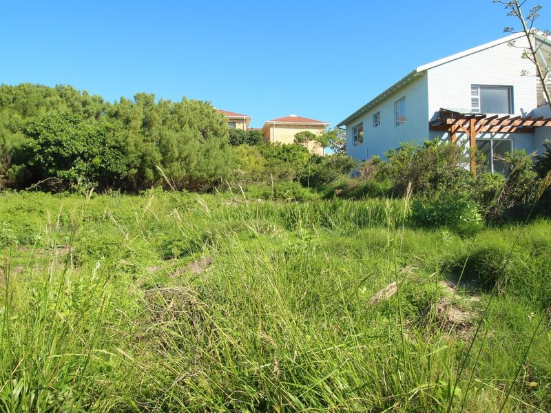 A view of a vacant residential plot featuring natural vegetation and sloped terrain, adjacent to an existing residential property.