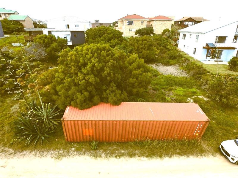 Aerial view of a vacant residential plot featuring a shipping container, mature trees, and surrounding residential properties.