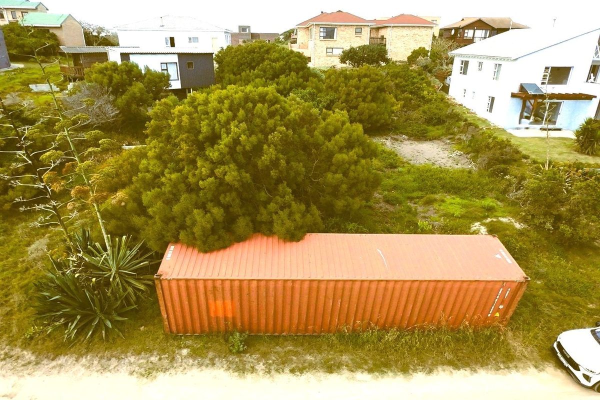 Aerial view of a vacant residential plot featuring a shipping container, mature trees, and surrounding residential properties.