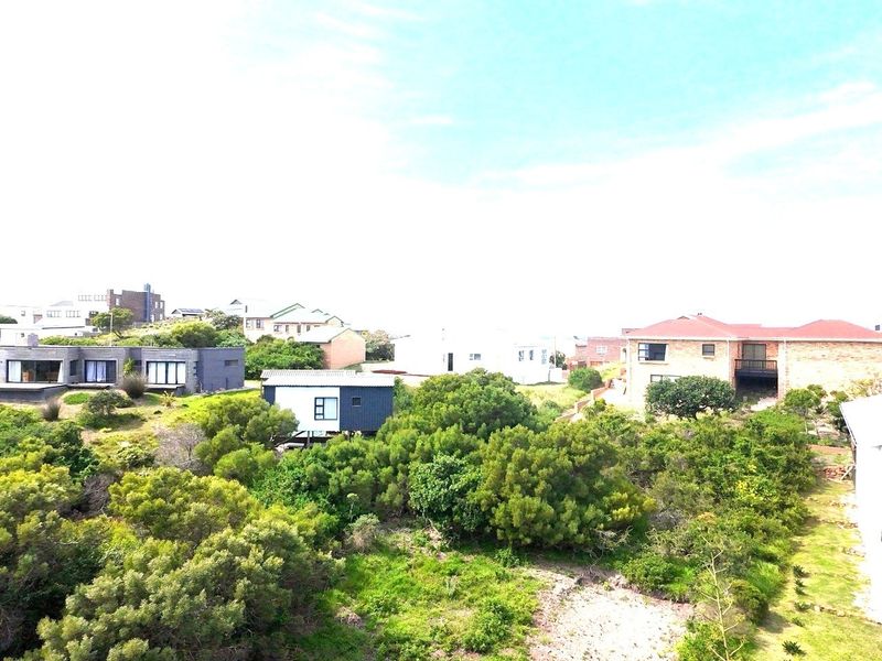 An aerial view of the residential neighborhood showing surrounding properties and established coastal vegetation on the vacant land.