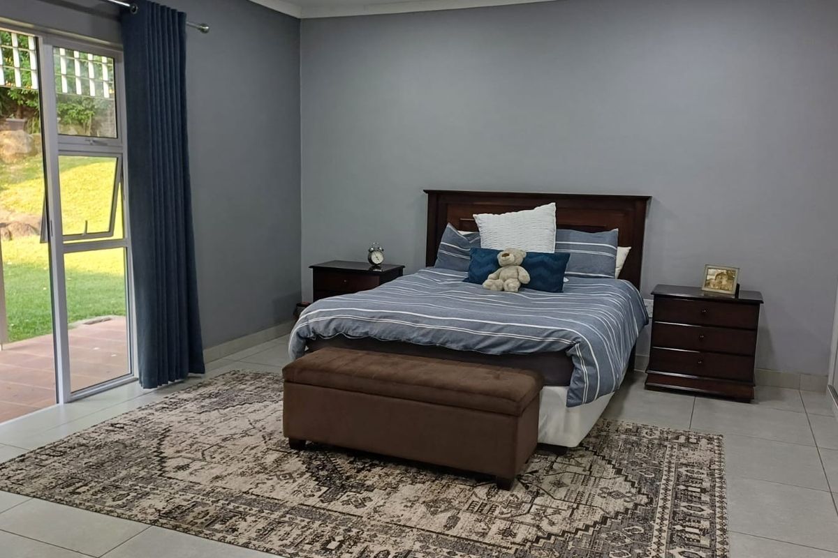 Spacious bedroom featuring neutral grey walls, tiled flooring, built-in cupboards, and a large sliding glass door providing direct access to the garden.
