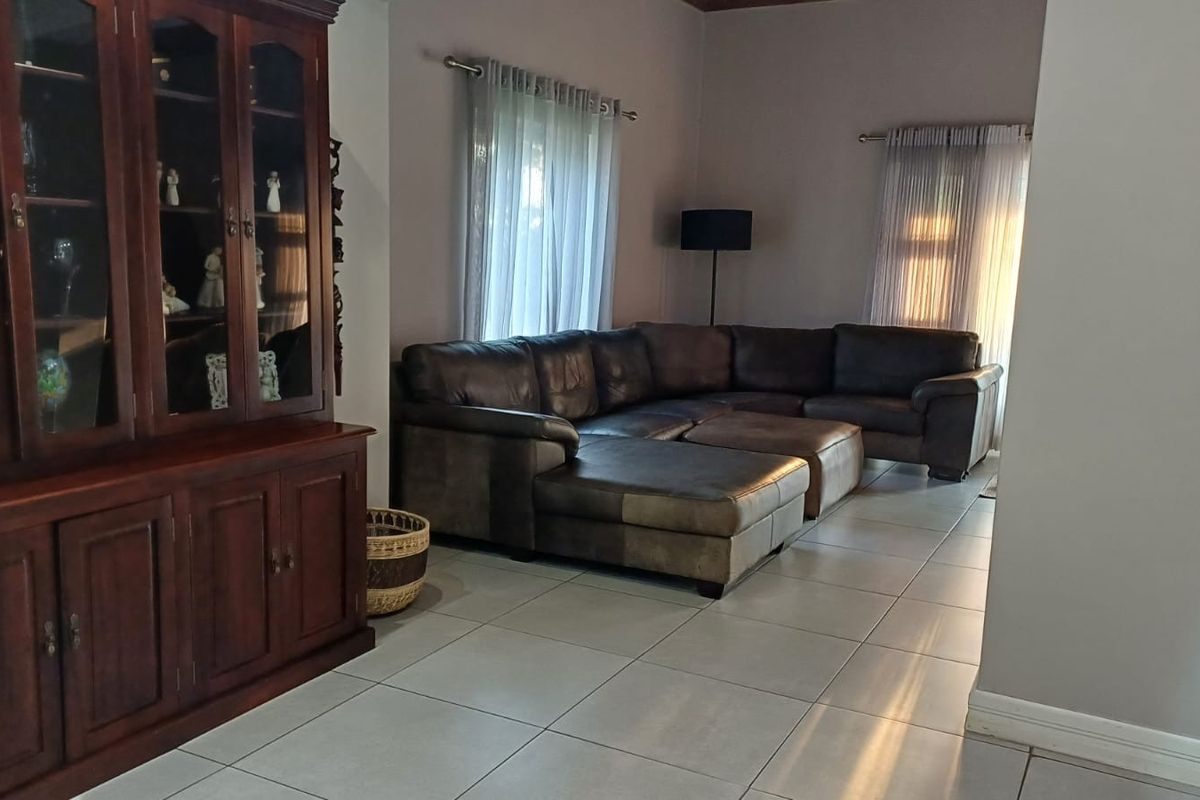 A spacious living room featuring neutral tiled flooring and natural light through large windows with curtain rods.