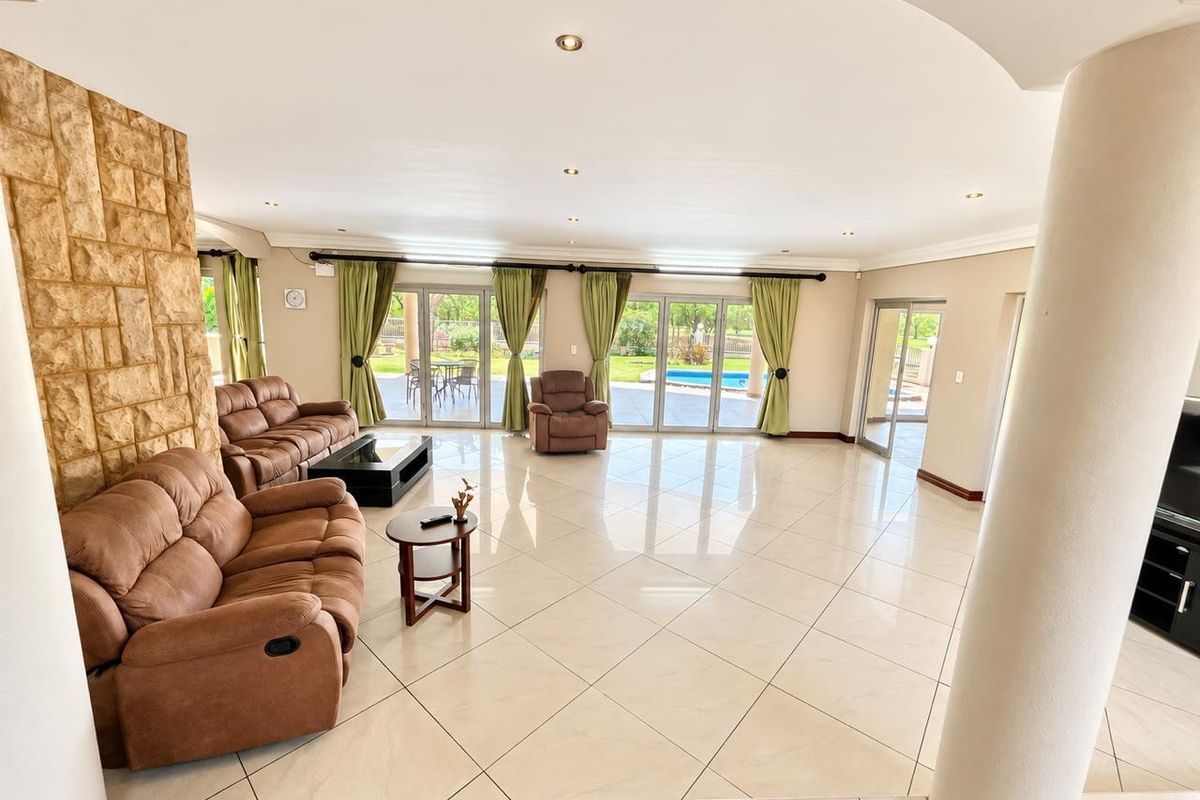 Spacious open-plan living area featuring large format floor tiles, a prominent stone feature wall, and multiple sliding glass doors providing access to the pool area.