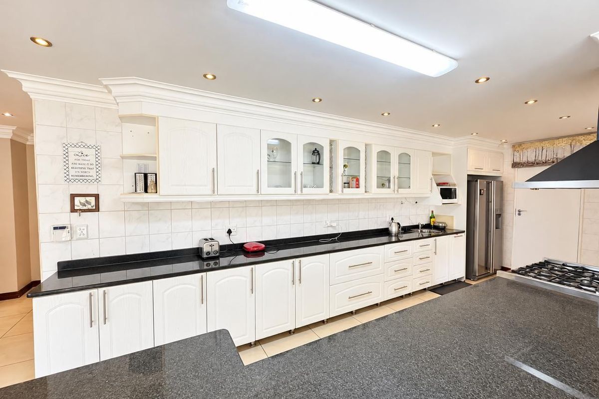Spacious kitchen featuring extensive white cabinetry, dark granite countertops, a gas hob with extractor fan, and ample workspace with integrated lighting.